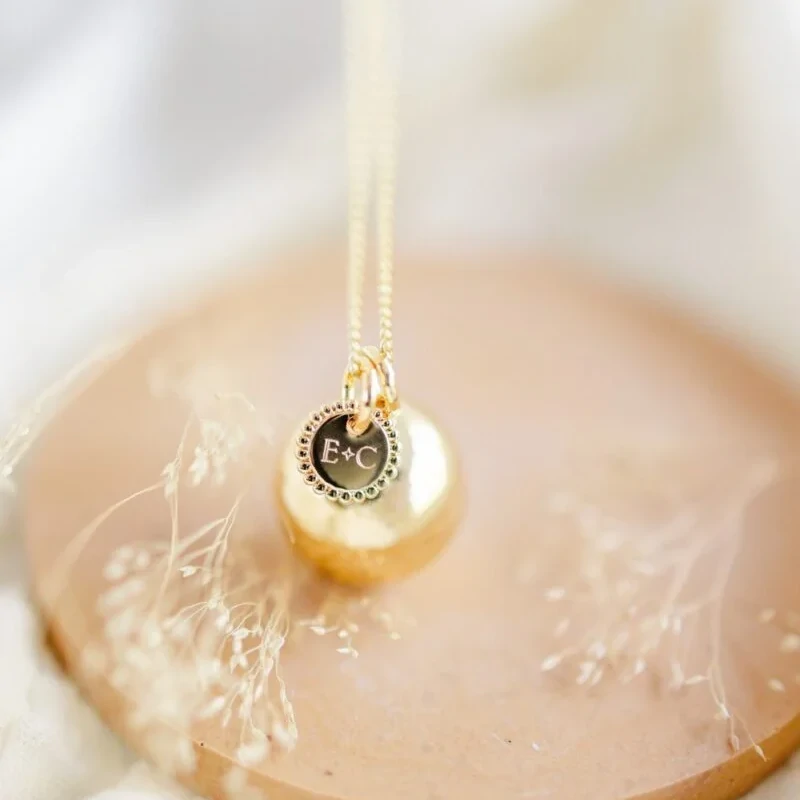 Bola de grossesse personnalisé avec initiales posé sur un ventre arrondi, bijou de maternité unique et souvenir de naissance