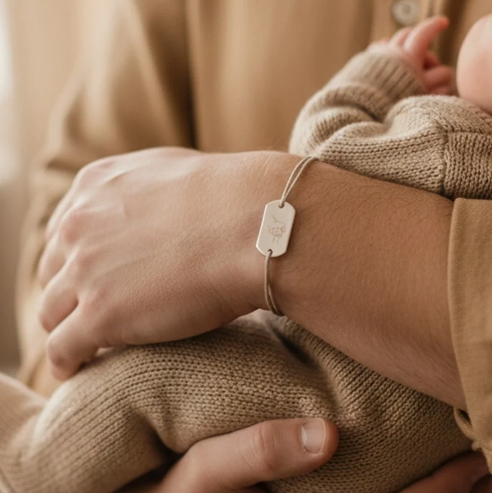 Bracelet homme personnalisé porté par un papa tenant son bébé, moment tendre et lien père-enfant