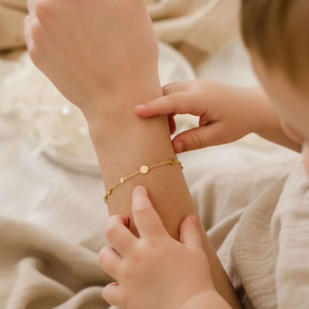 Bracelet fin personnalisé avec initiales porté par une maman, moment tendre avec un enfant dans une ambiance douce et naturelle