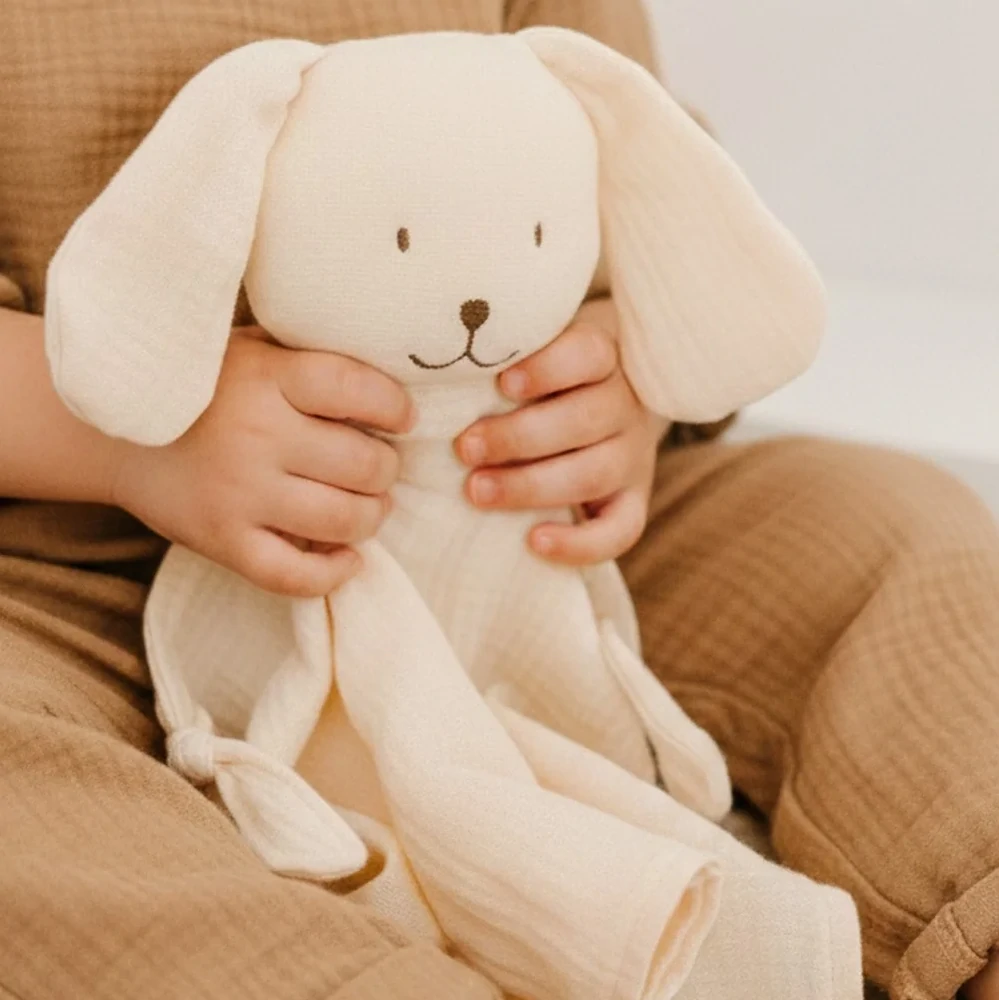 Bébé tenant un doudou chien en tissu doux, compagnon rassurant pour nouveau-né dans un univers chaleureux